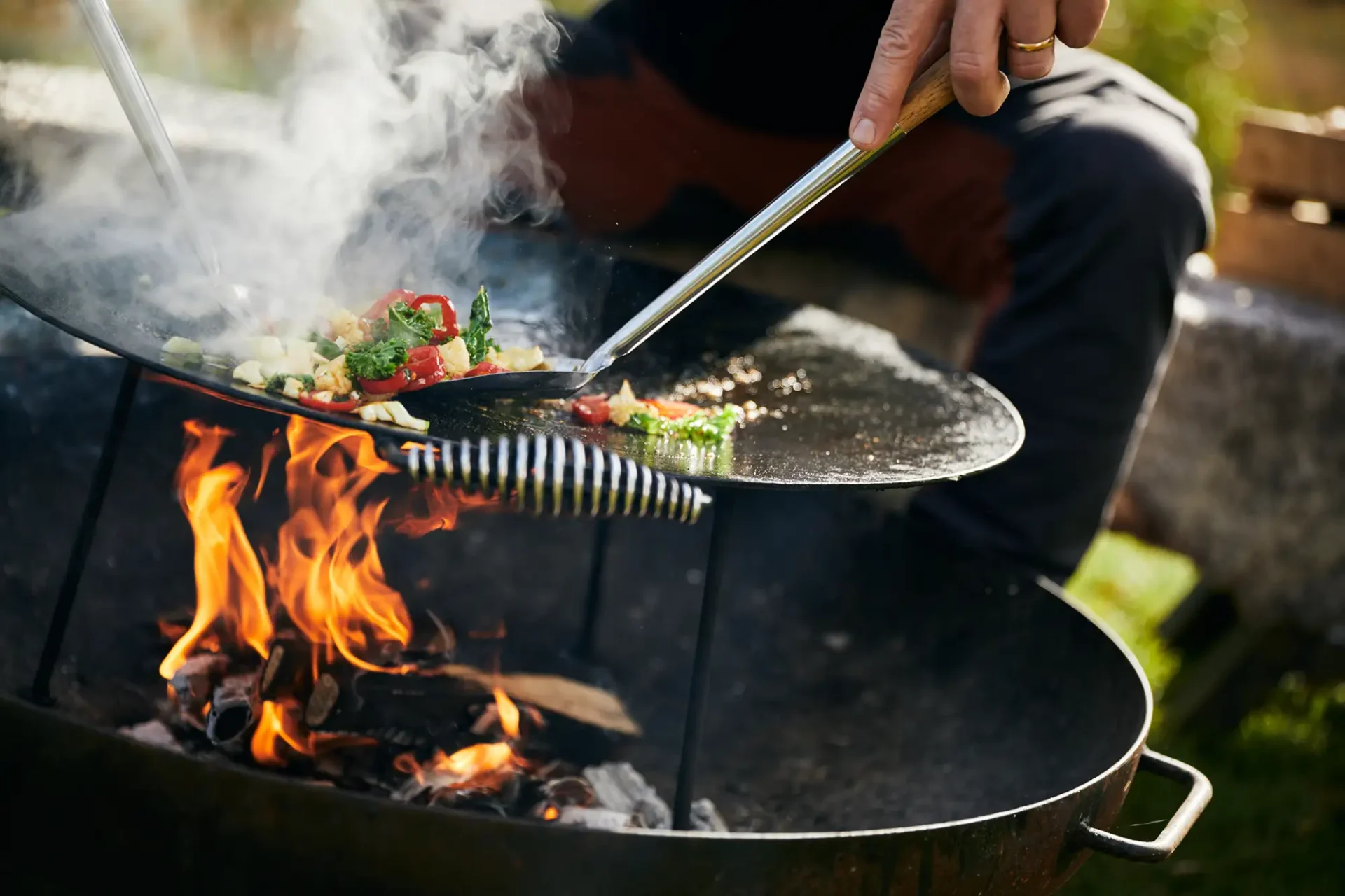Outdoor cooking where vegetables are prepared over an open fire on a griddle.