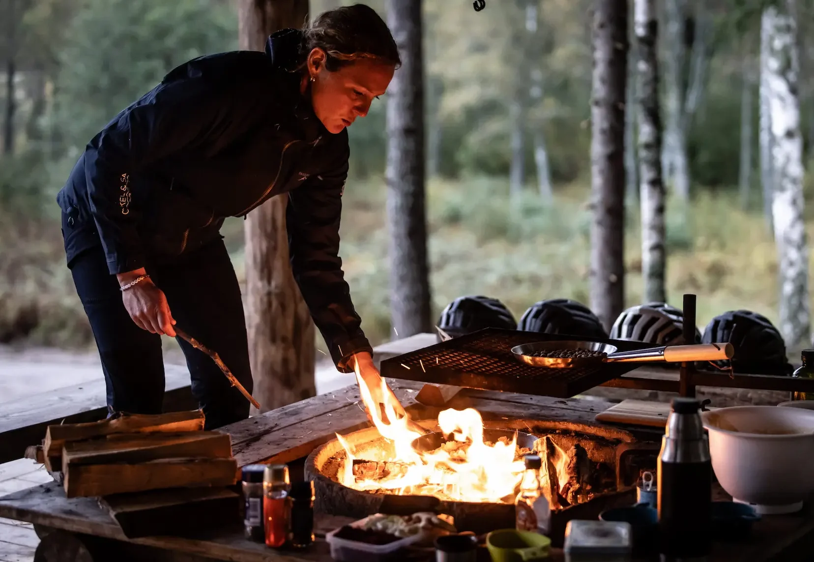 Naturupplevelser i Västra Götaland - Person vid lägereld i skogsmiljö som lagar mat utomhus, med campingutrustning på ett träbord. Foto: Robert Dahlberg.
