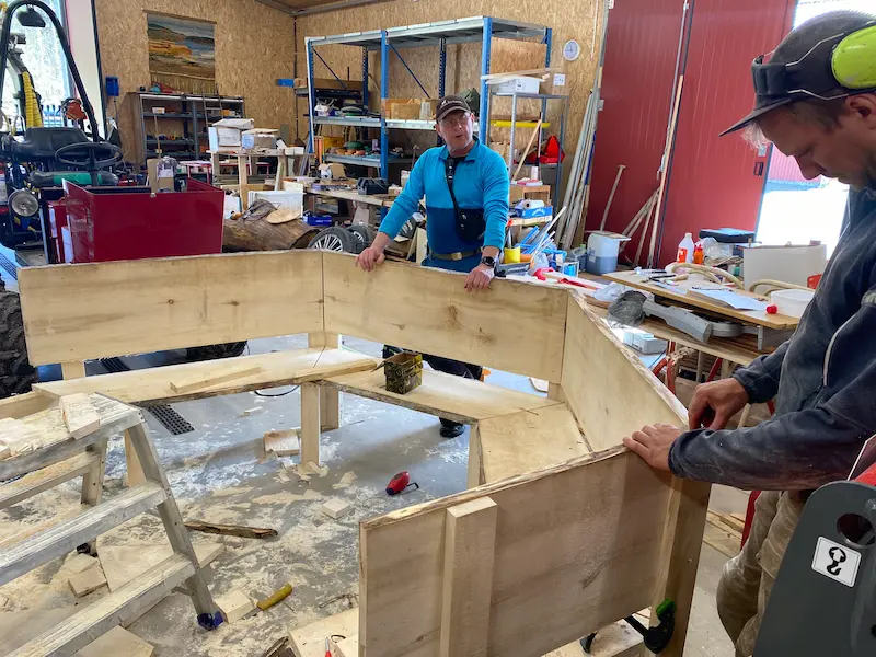 Två personer som bygger specialanpassade bastubänkar i trä för ett sexkantigt bastutält.