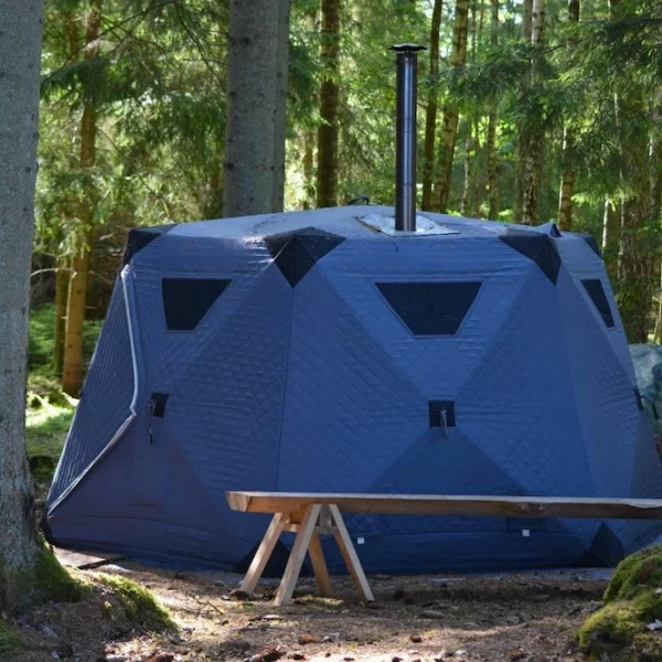 Vedeldat bastutält uppställt i skogen, omgivet av träd och natur.