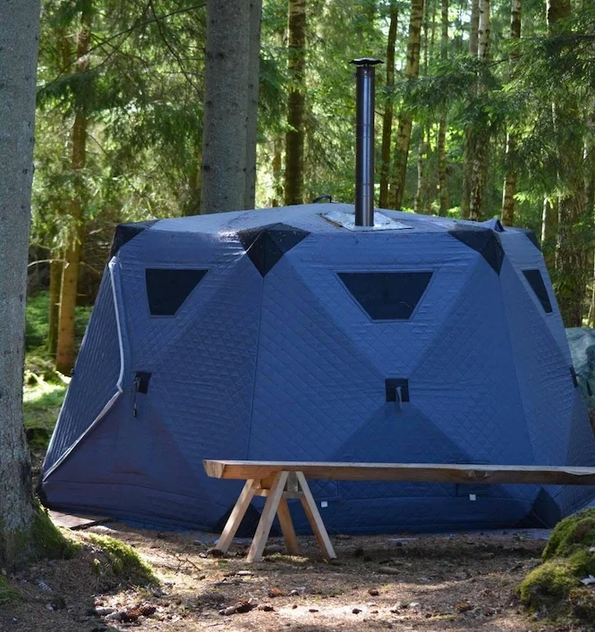 Vedeldat bastutält uppställt i skogen, omgivet av träd och natur.