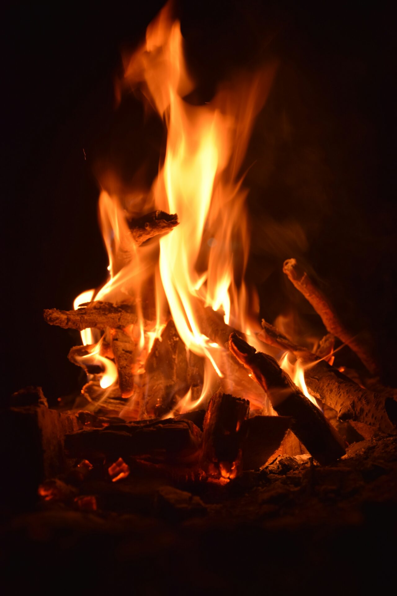 Sprakande lägereld med flammande ved i mörker – symbol för värme och gemenskap.