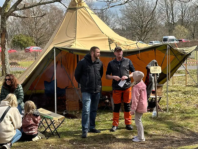 Peter Carlsson samtalar med besökare vid ett tipi-tält under Kungsbacka Outdoor Festival, med barn och vuxna i bakgrunden.